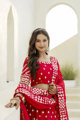 Woman in a red traditional outfit with white patterns standing in front of arched stone walls.