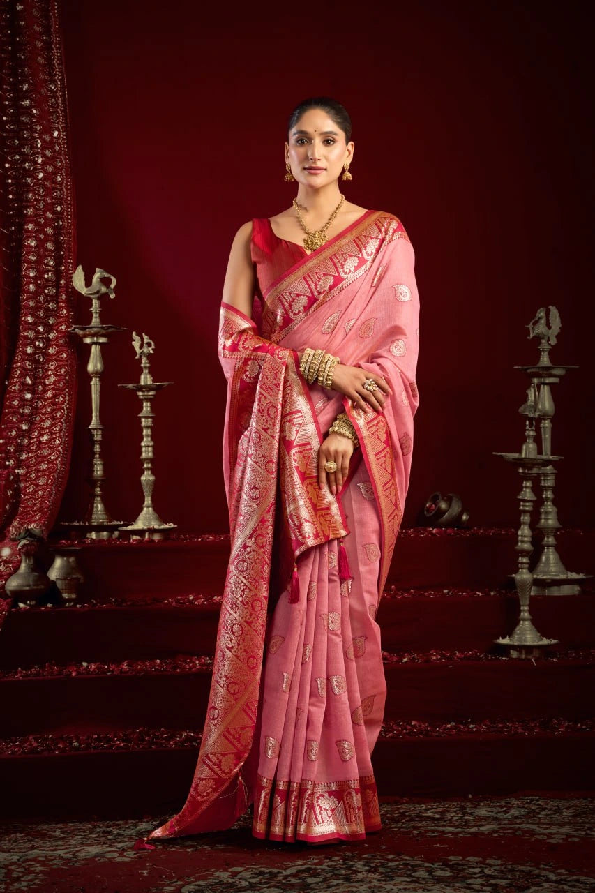 Woman in a pink saree with intricate patterns against a red background