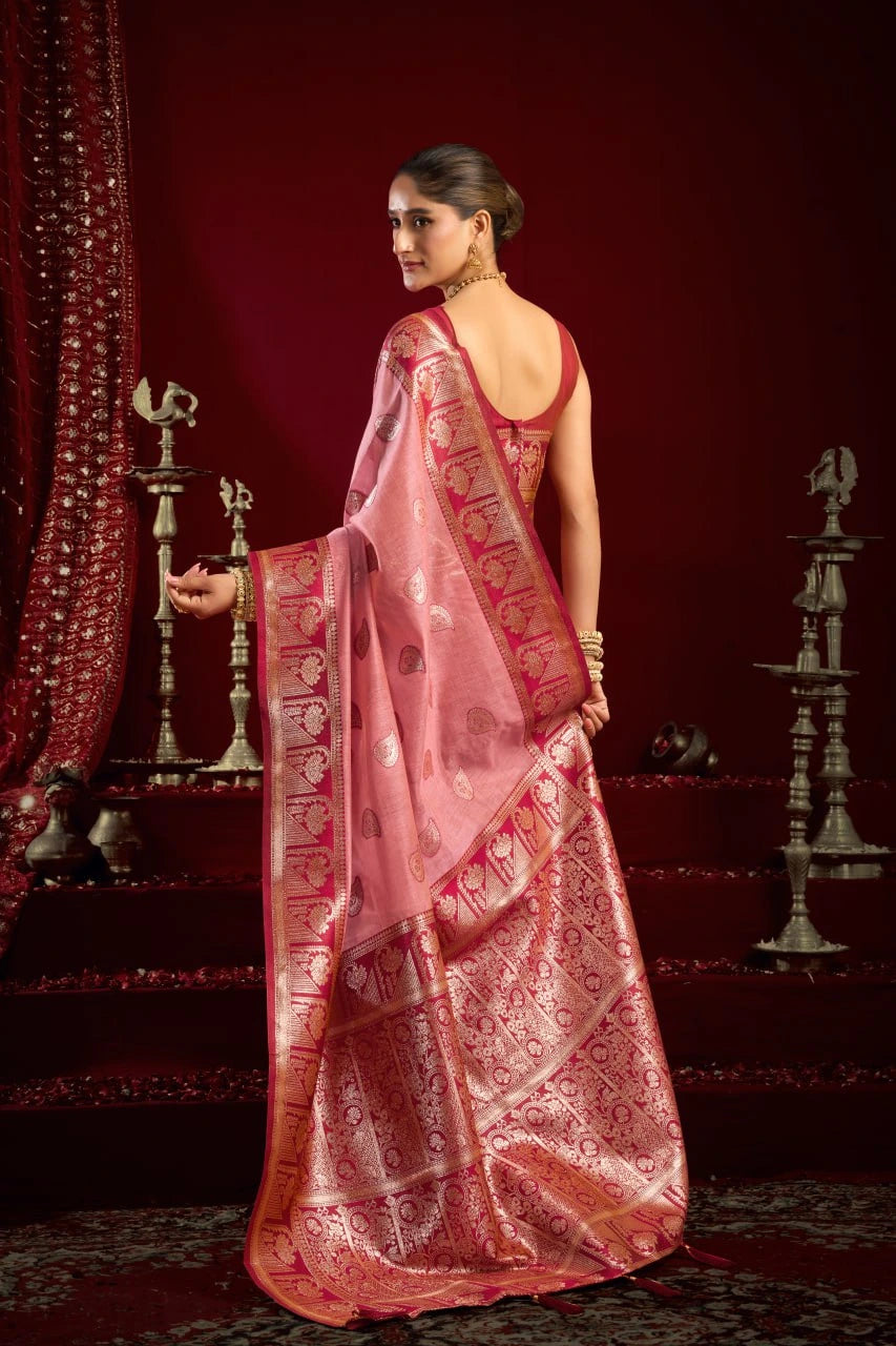 Woman in a pink saree with intricate patterns against a red background