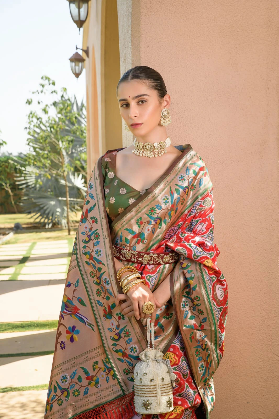 Woman in a traditional saree with a decorative bag outdoors.
