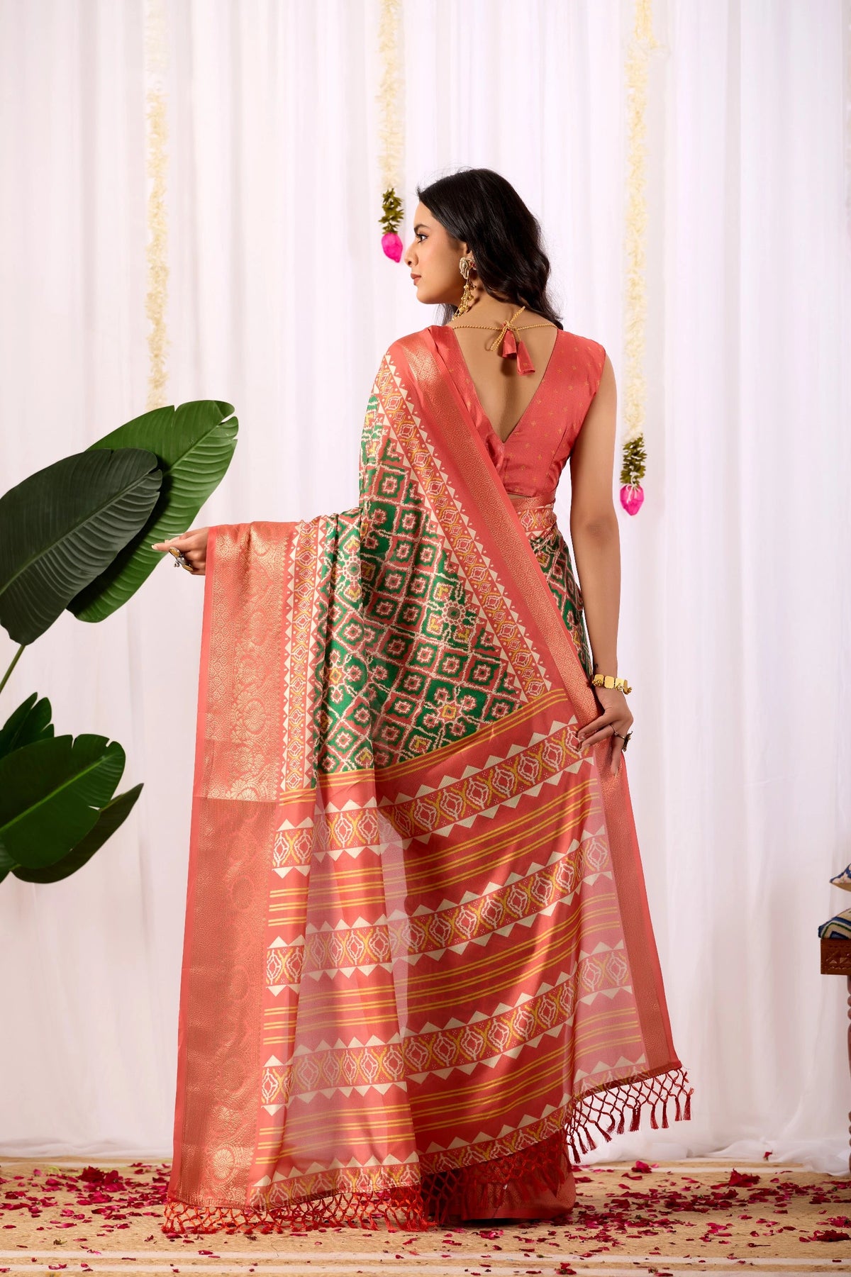 Woman holding a traditional saree with a white curtain and plant in the background