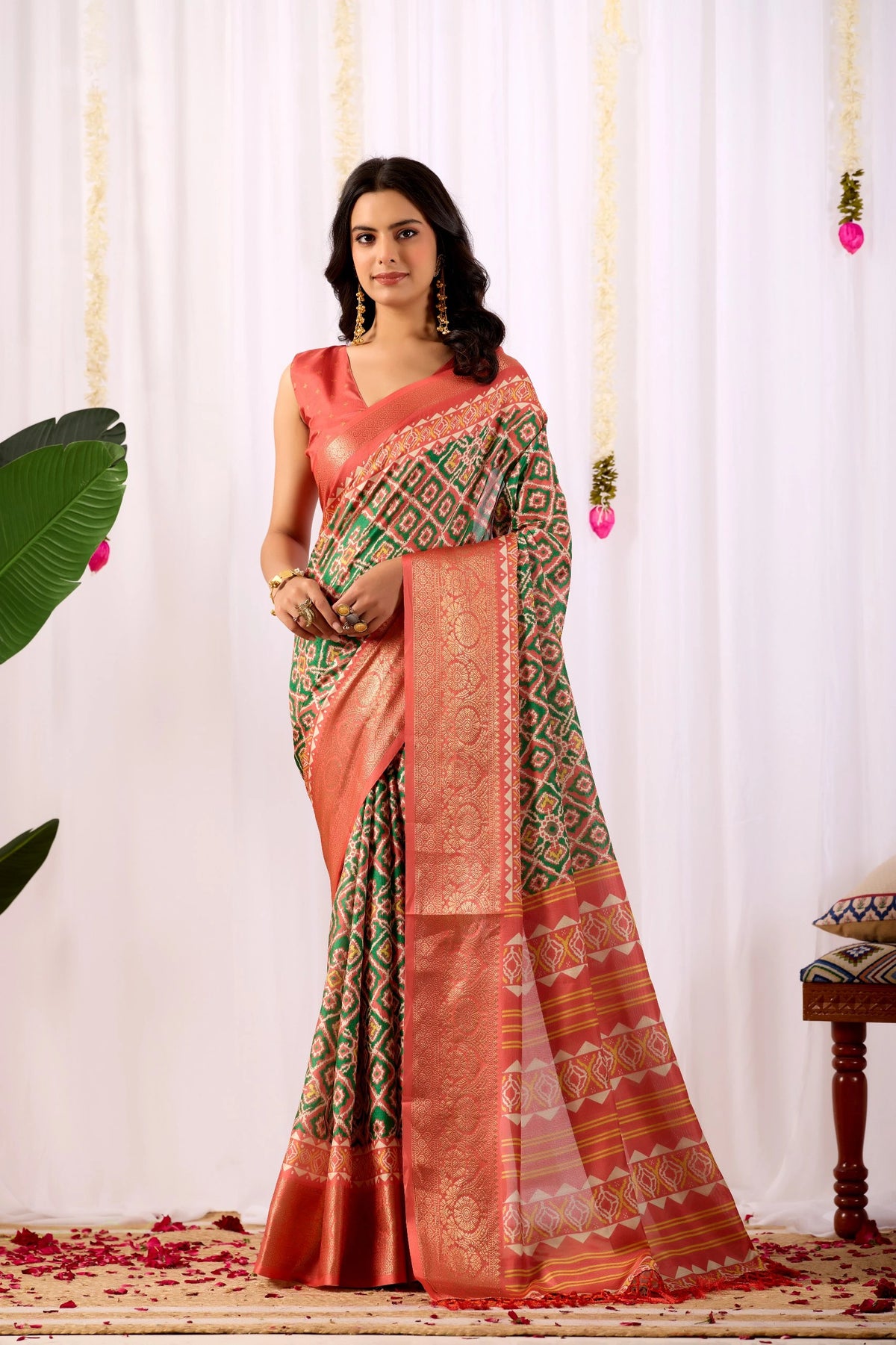 Woman wearing a traditional saree with a green and orange pattern against a white curtain background