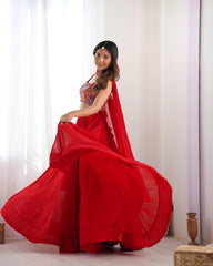 Woman in a red saree standing in a well-lit room with white curtains.
