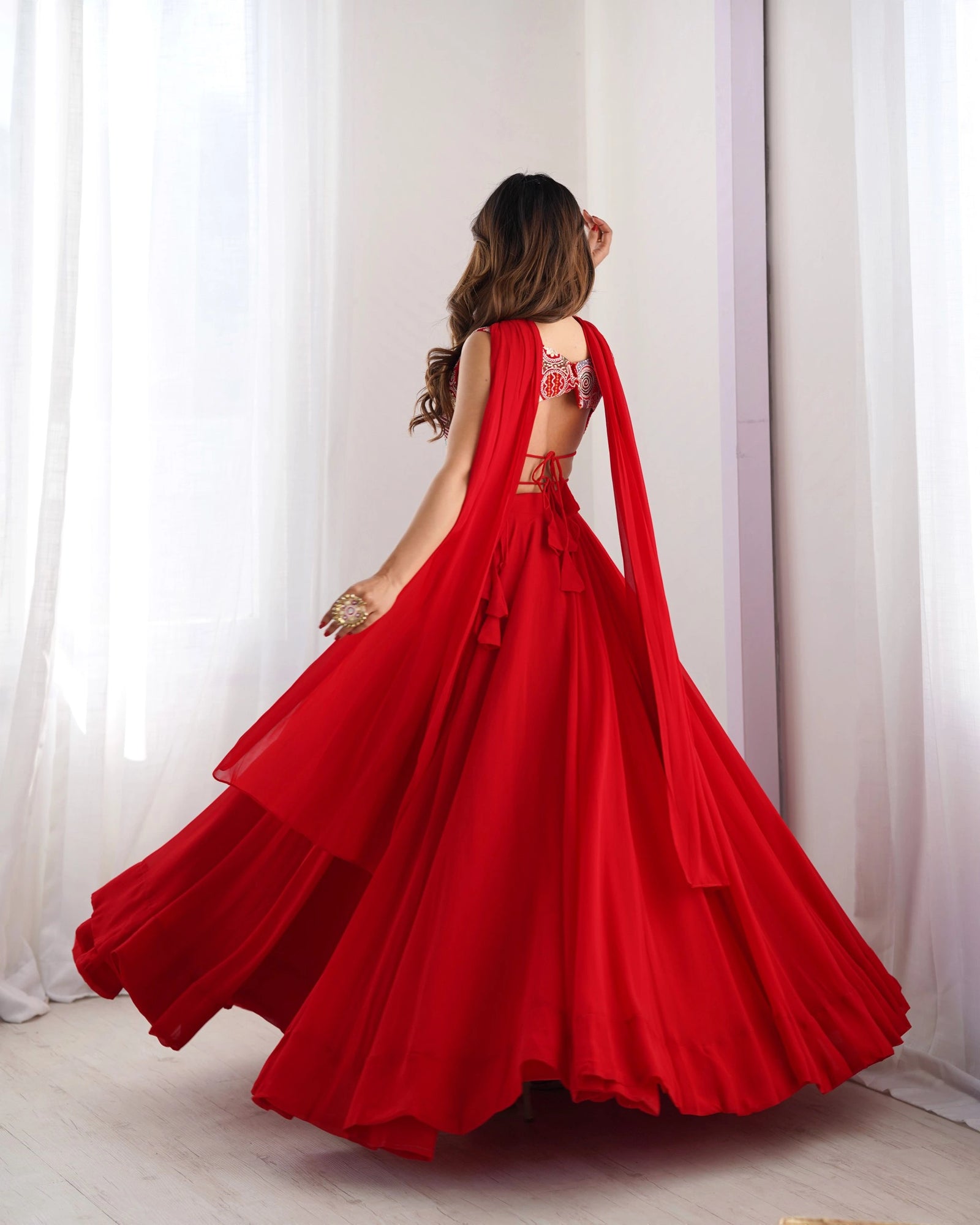 Woman wearing a red evening gown with a cape in front of white curtains