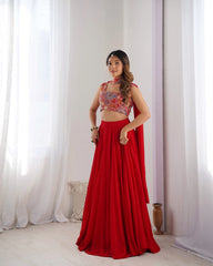 Woman wearing a red and patterned top with a long skirt against a white curtain background