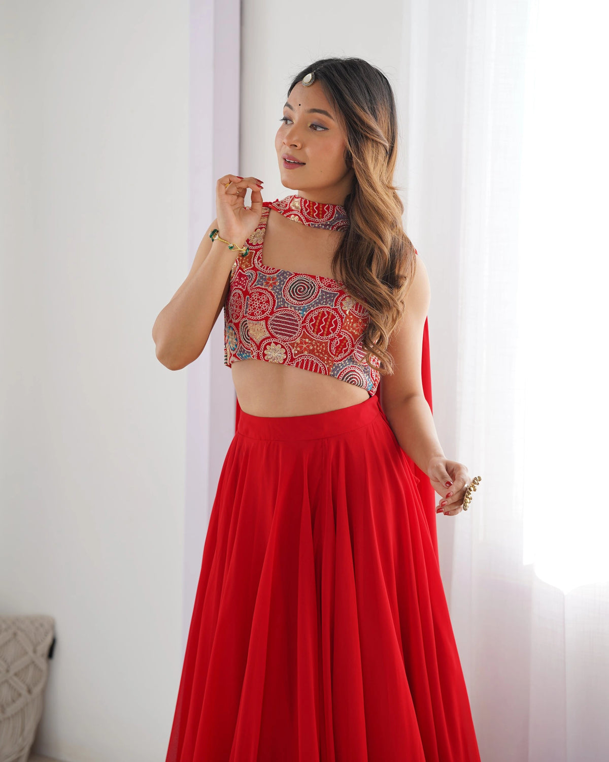 Woman wearing a red traditional outfit with a patterned top against a white curtain background