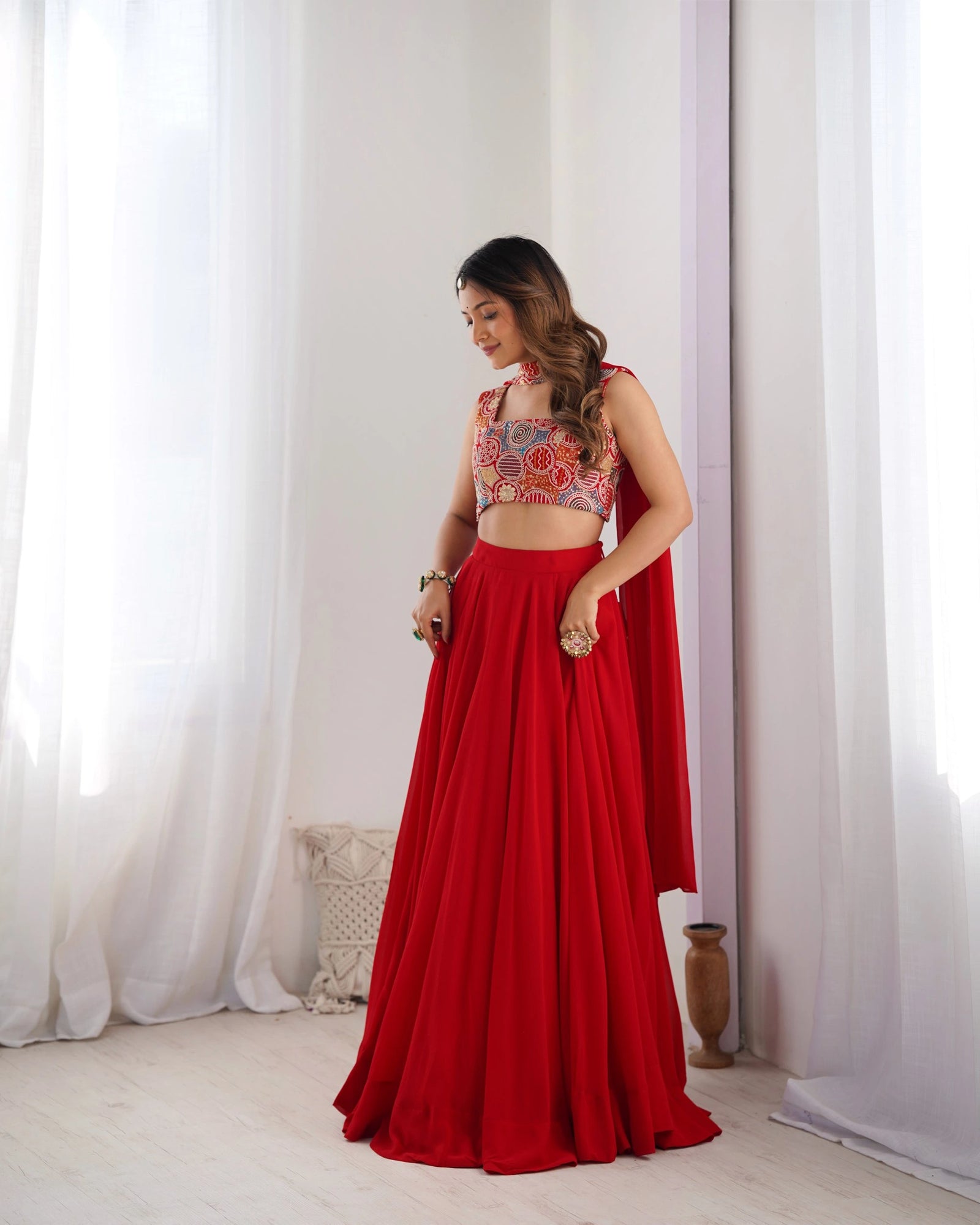 Woman wearing a red traditional outfit with a patterned top in a room with white curtains.