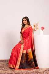 Woman wearing a red saree with gold border sitting on a white pedestal.