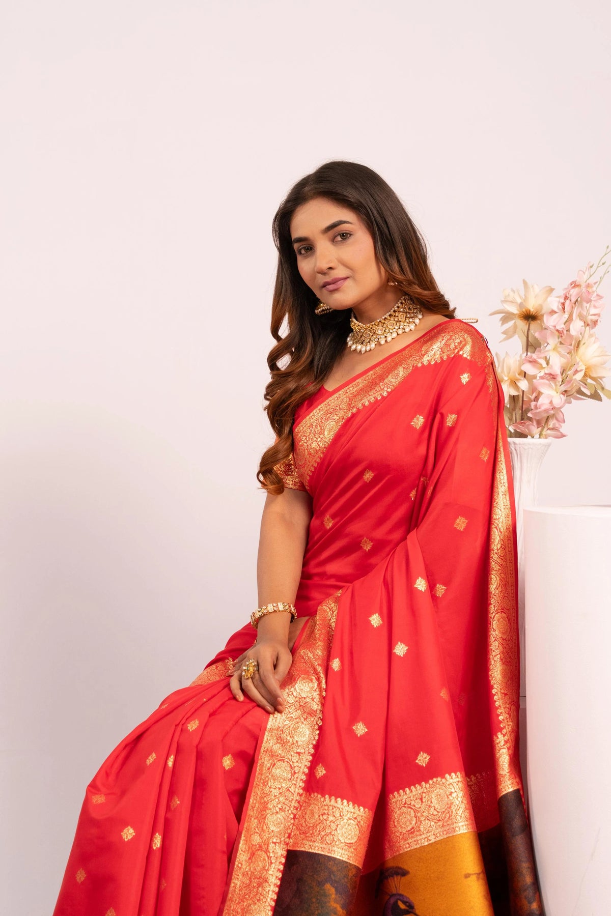 Woman wearing a red saree with gold patterns on a white background