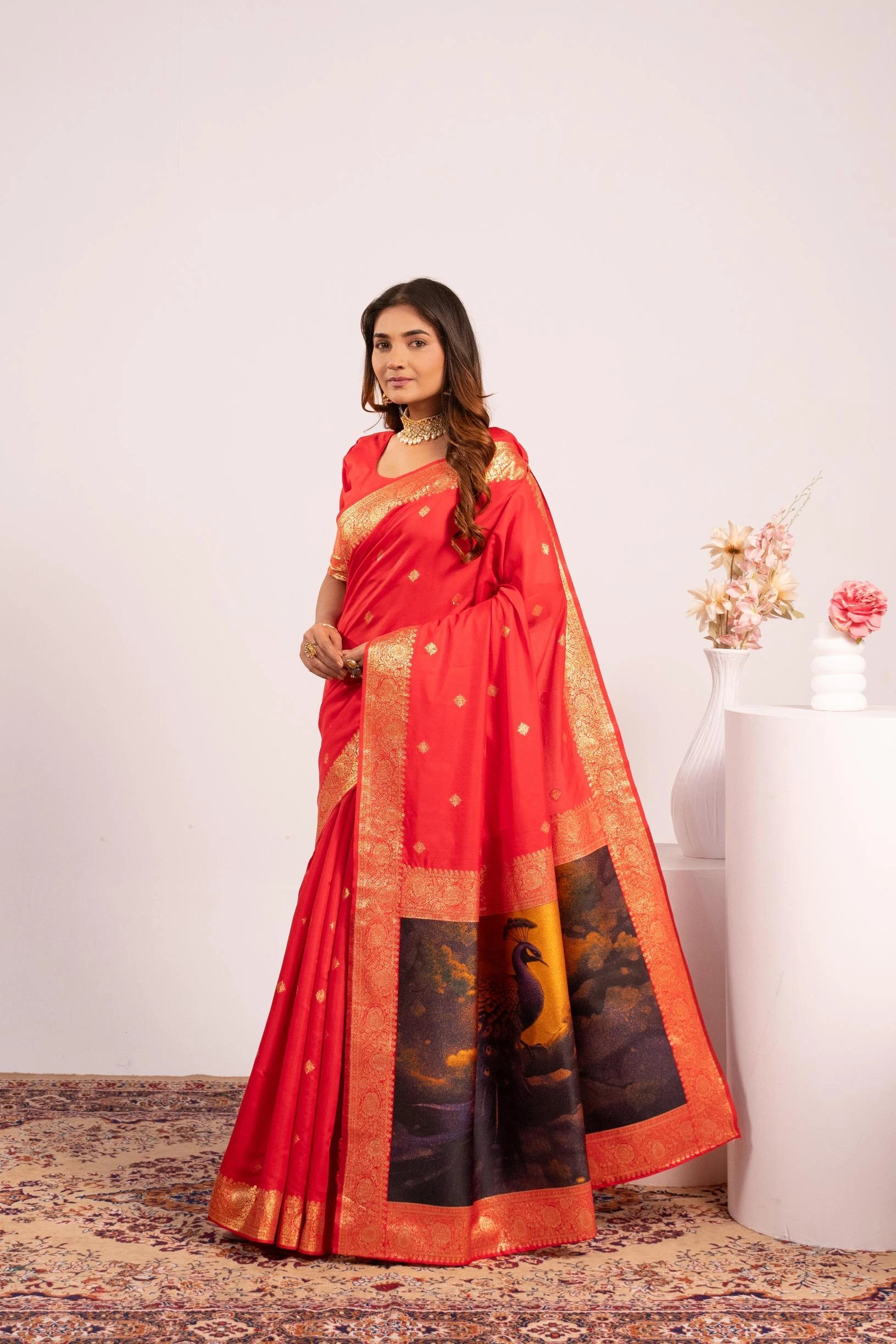 Woman wearing a red saree with a black and gold border, standing against a white background.