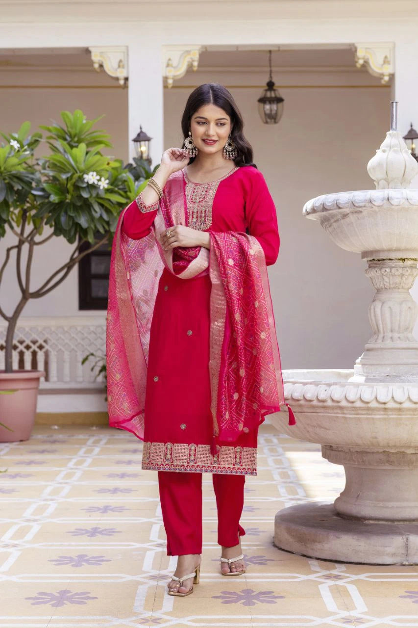 Woman in a red traditional outfit standing in an outdoor setting with decorative elements.