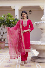 Woman in a pink traditional outfit standing in an outdoor setting with decorative elements.