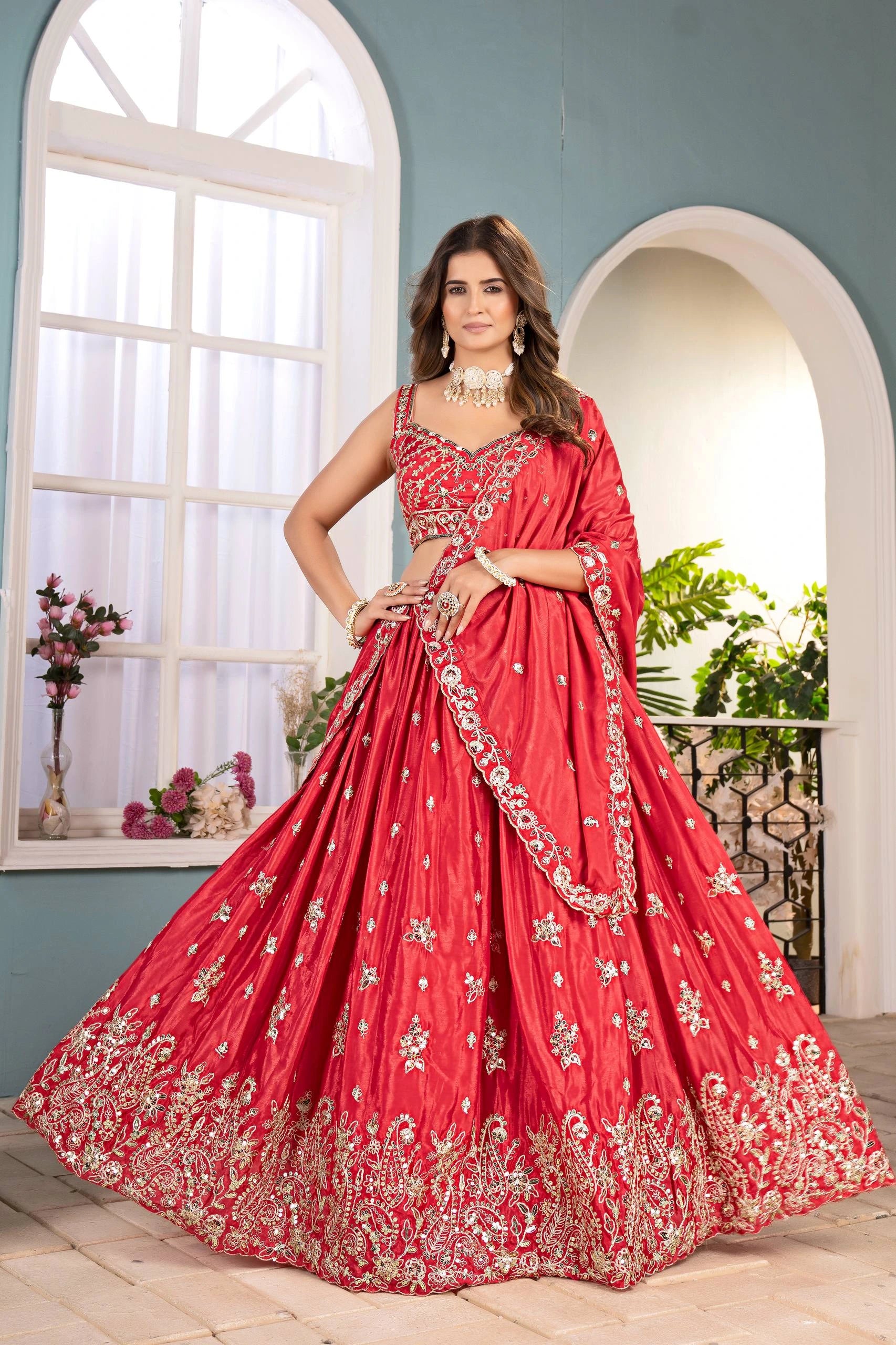 Woman in a red embroidered traditional dress standing in a well-lit room with plants.