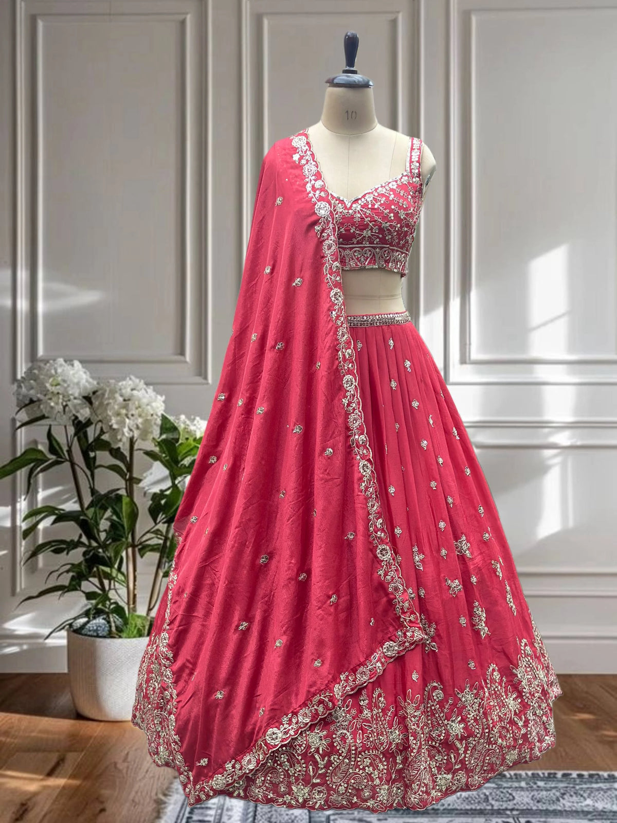 Pink embroidered lehenga on a mannequin against a white paneled wall.