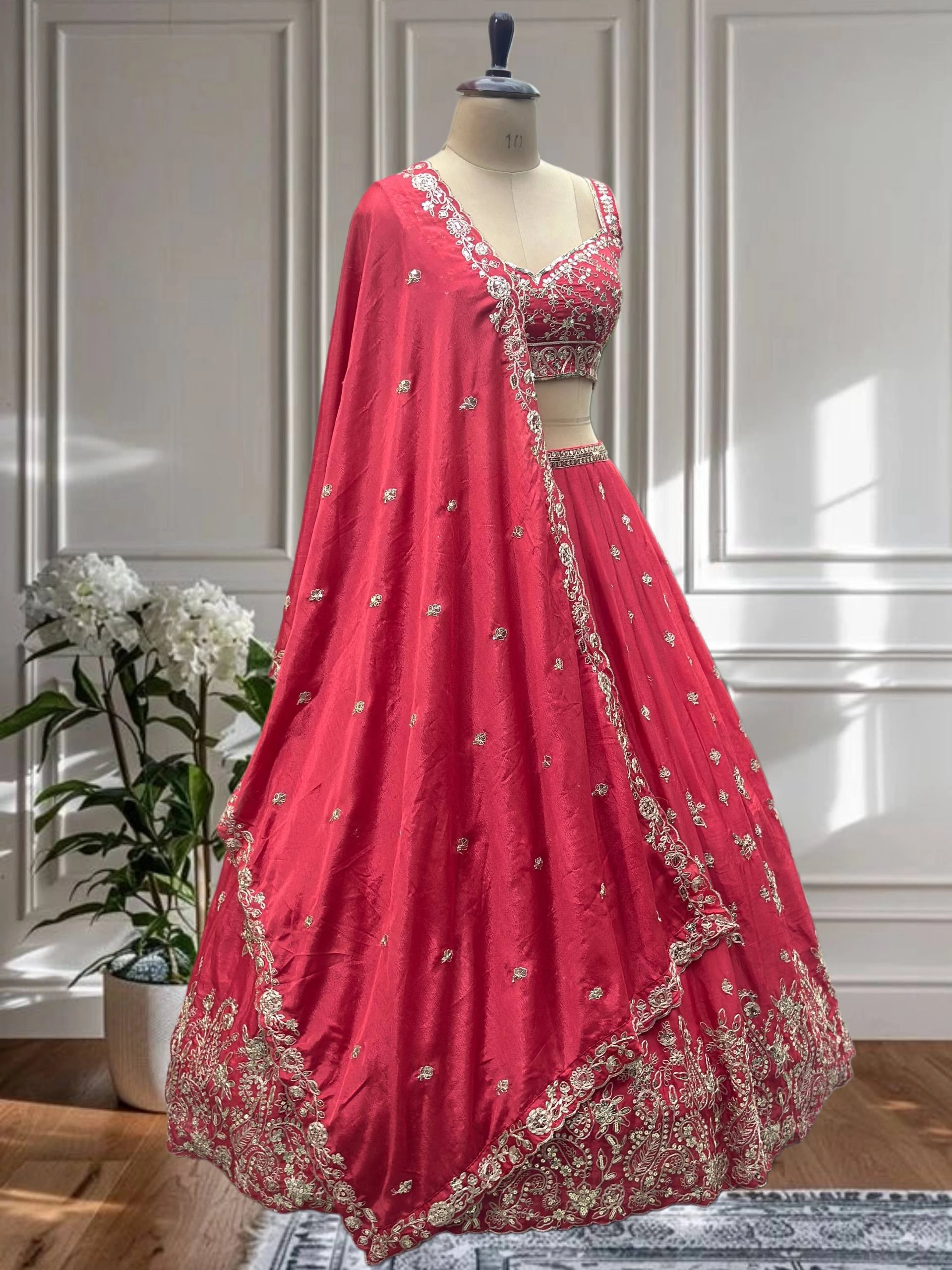 Red embroidered lehenga on a mannequin against a white paneled wall.
