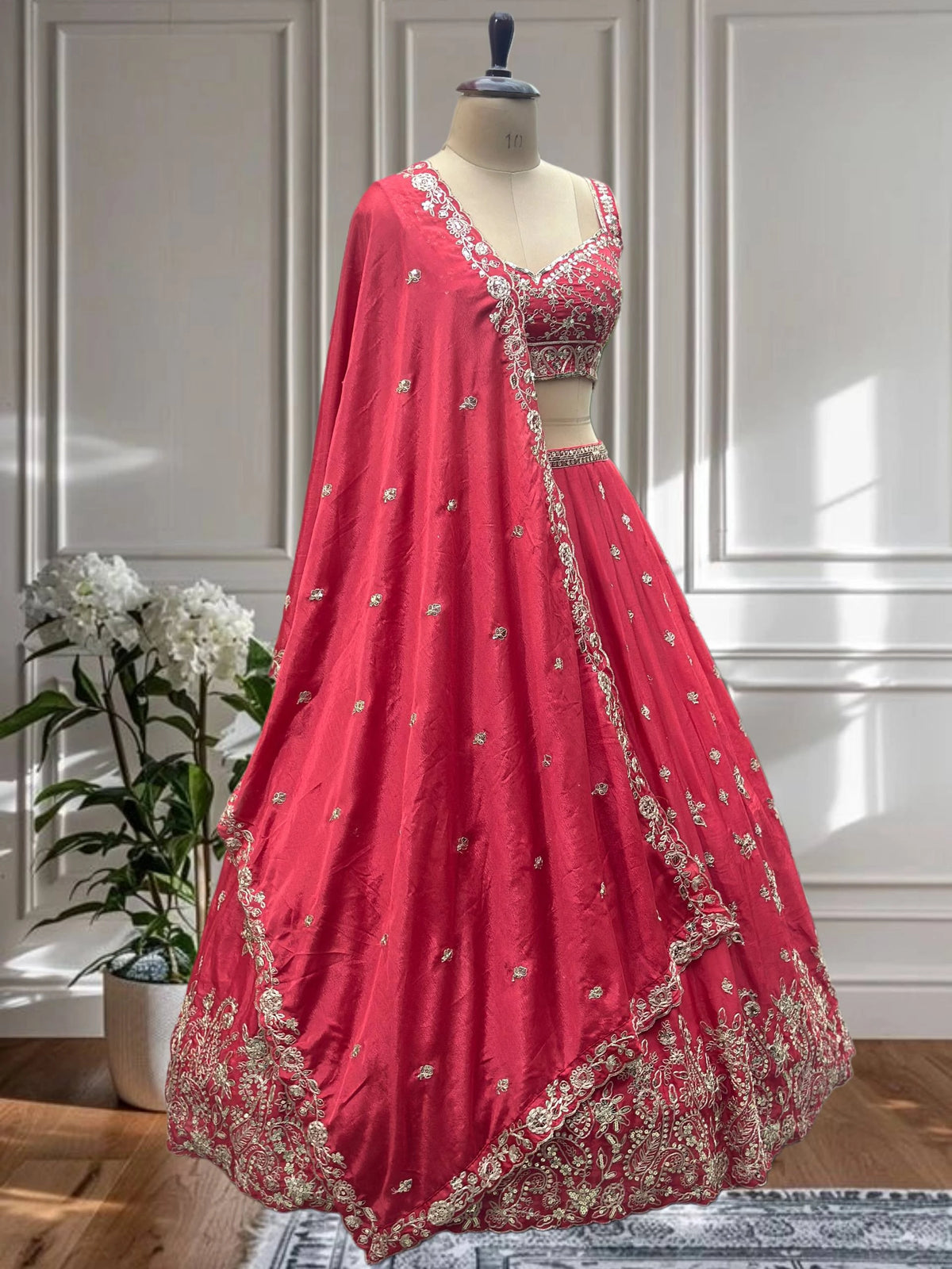 Red embroidered lehenga on a mannequin against a white paneled wall.