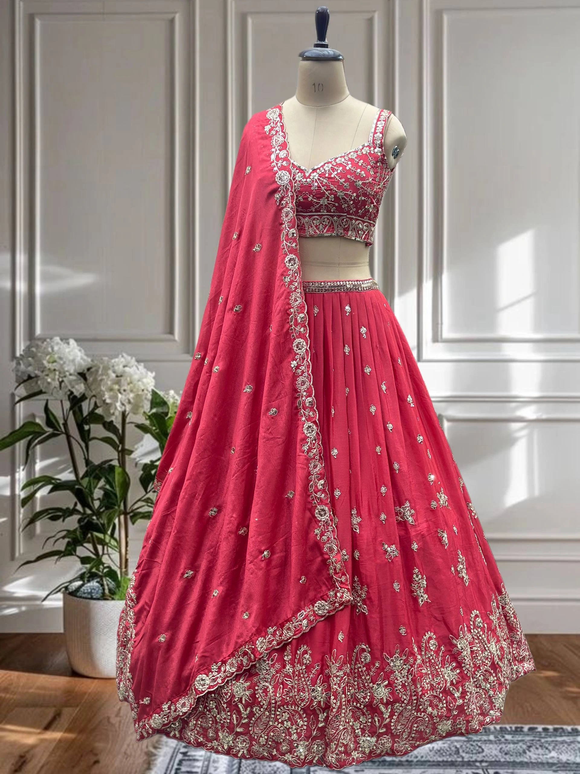 Pink embroidered lehenga on a mannequin against a white paneled wall.