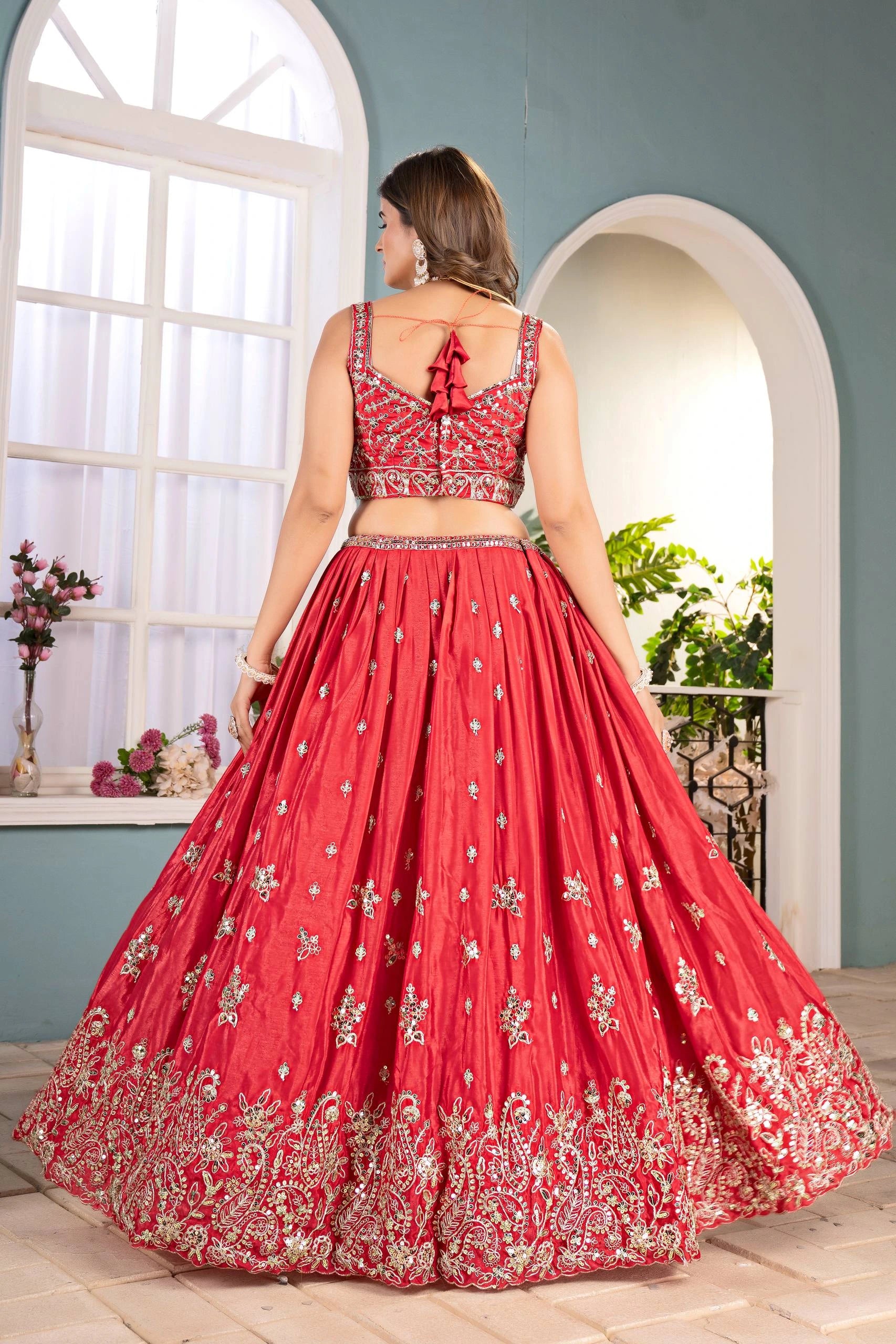 Woman in a red embroidered traditional outfit standing in a bright room with large windows.