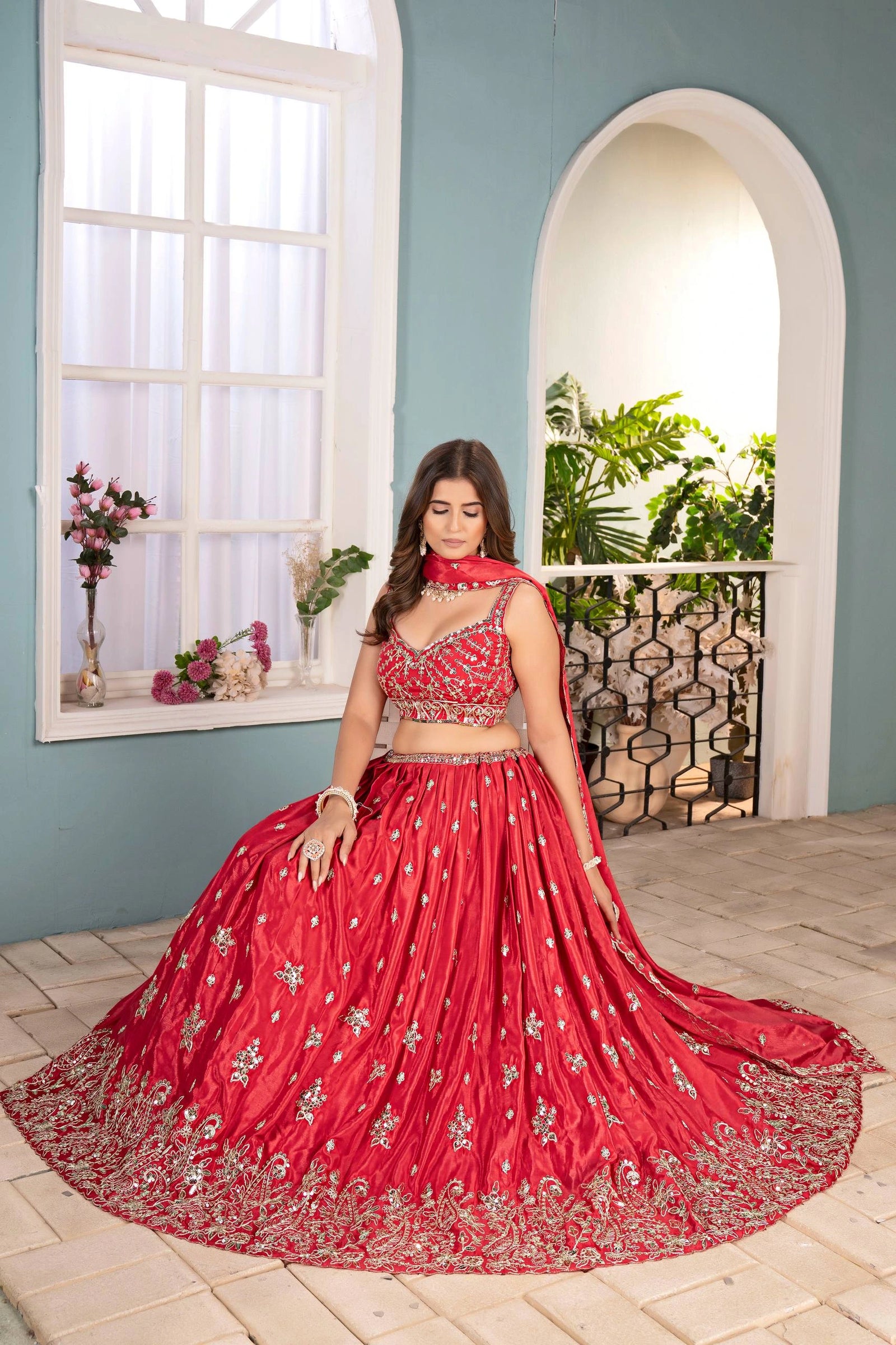 Woman in a red embroidered traditional outfit standing in a room with light blue walls and a window.