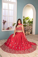 Woman in a red embroidered traditional outfit standing in a room with light blue walls and a window.