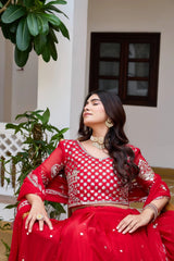 Woman in a red traditional outfit sitting indoors with plants around