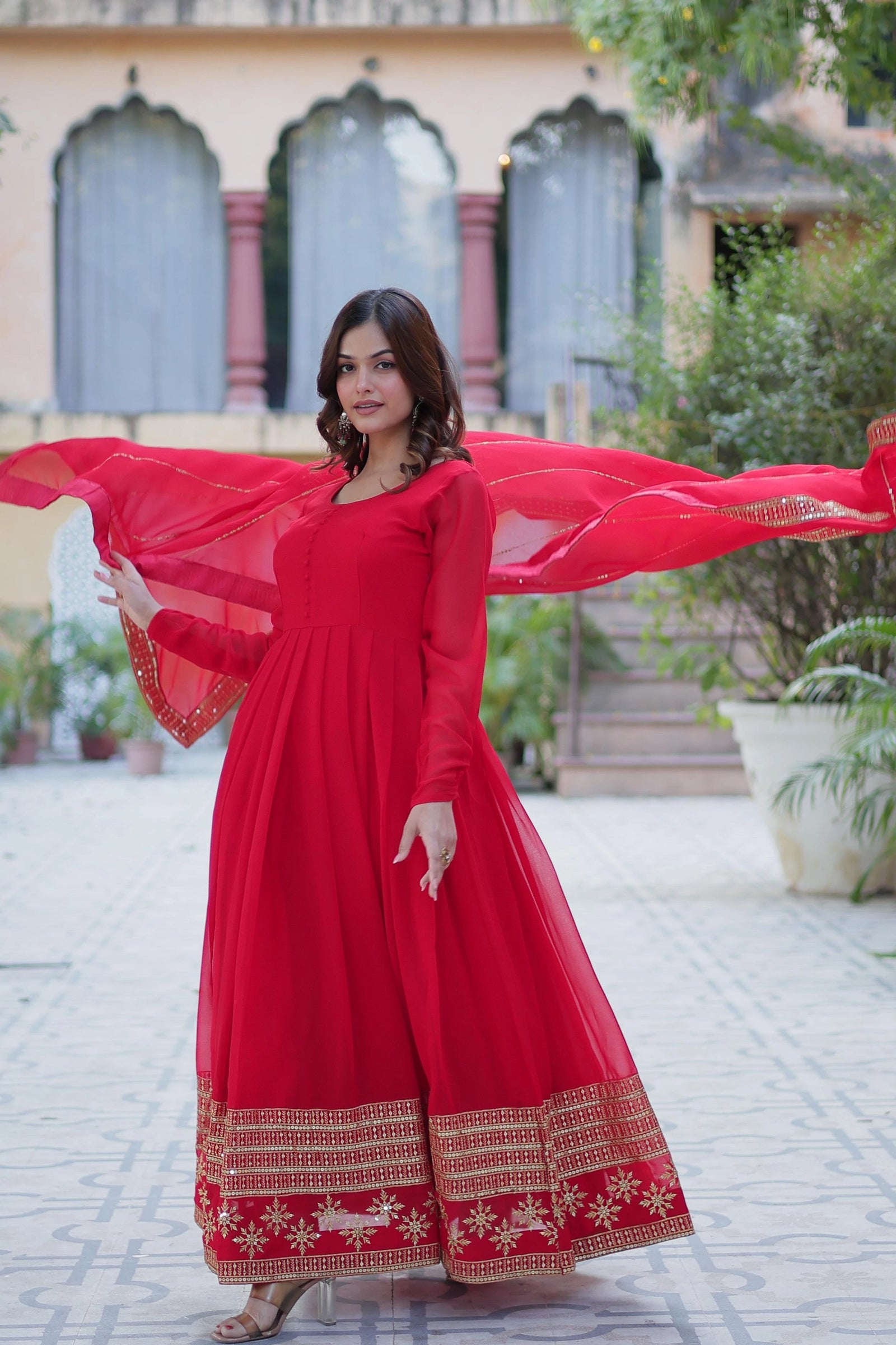 Woman in a red traditional outfit with a long dress and red dupatta, standing outdoors.