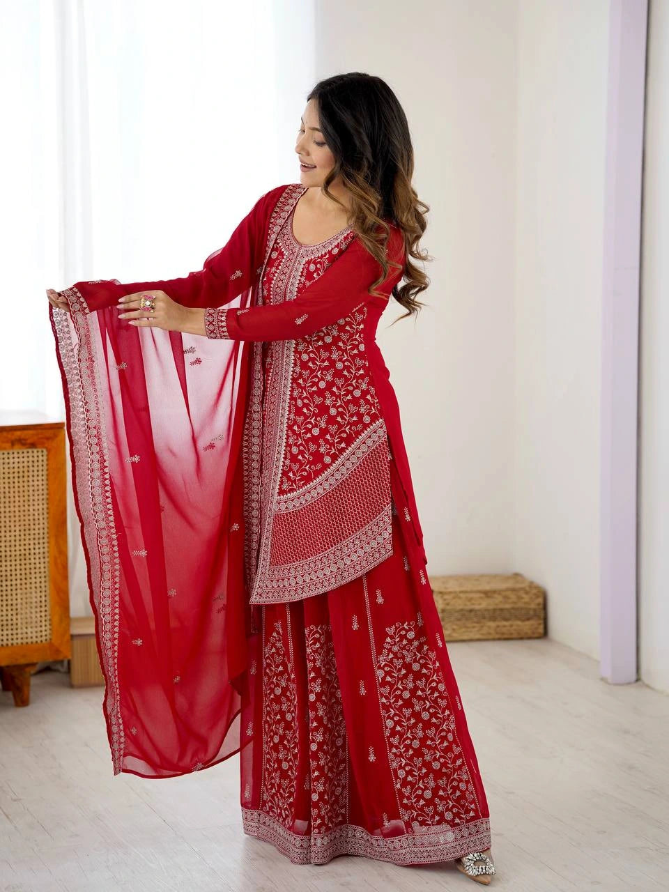 Woman in a red traditional outfit with white patterns in a minimalistic room.
