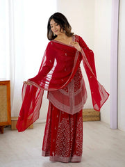 Woman wearing a red traditional outfit with a matching dupatta in a minimal indoor setting.