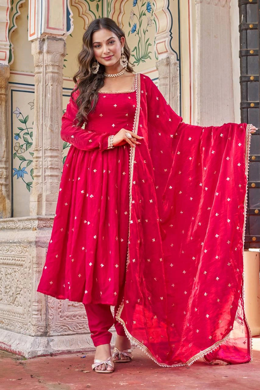 Woman in a red traditional outfit with a matching dupatta standing in front of an ornate wall.