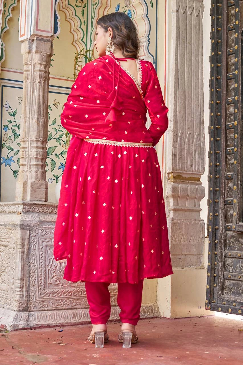 Woman wearing a red traditional outfit with white patterns in an ornate setting.
