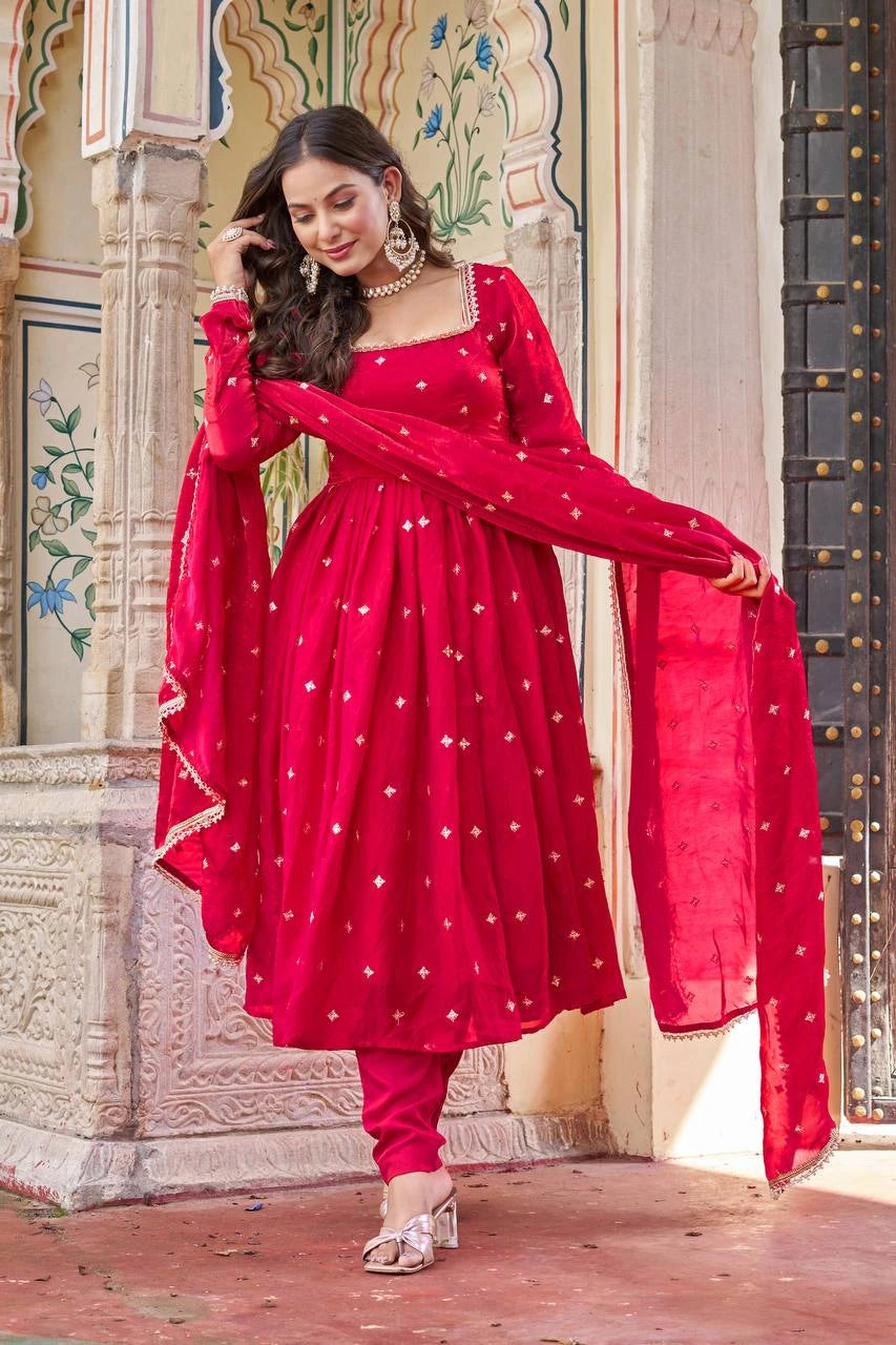 Woman in a red traditional outfit with white patterns standing in front of an ornate architectural background.