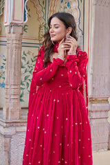 Woman in a red dress with white patterns standing in front of an ornate architectural background.