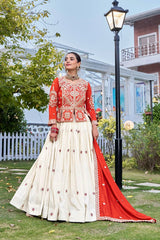 Woman in a red and white traditional outfit standing outdoors with greenery and a building in the background.