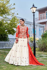Woman in a red and white traditional outfit standing outdoors with greenery and a building in the background.