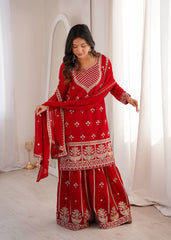Woman wearing a red traditional outfit with white patterns in a bright room.