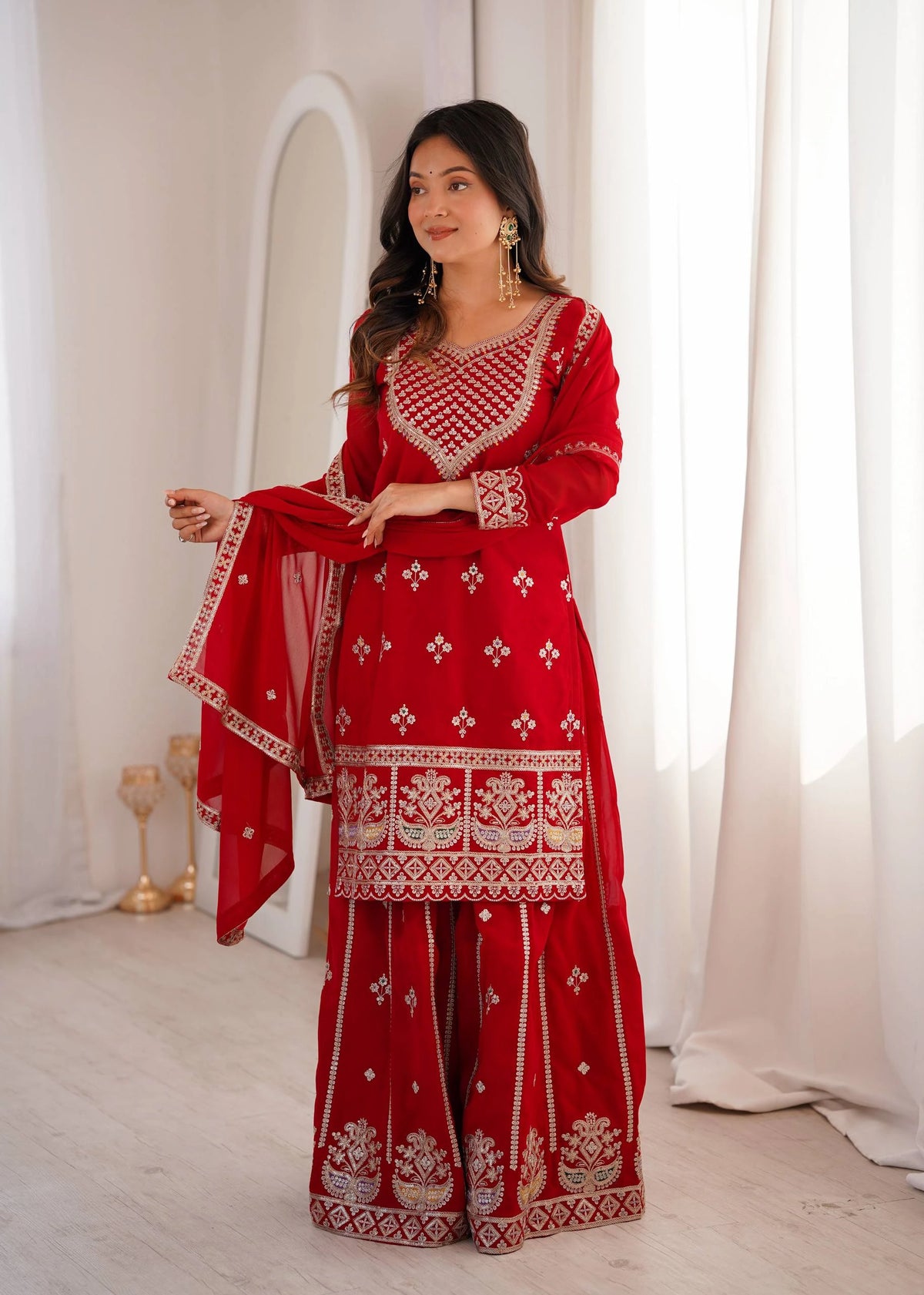 Woman wearing a red traditional outfit with white patterns in a bright room.