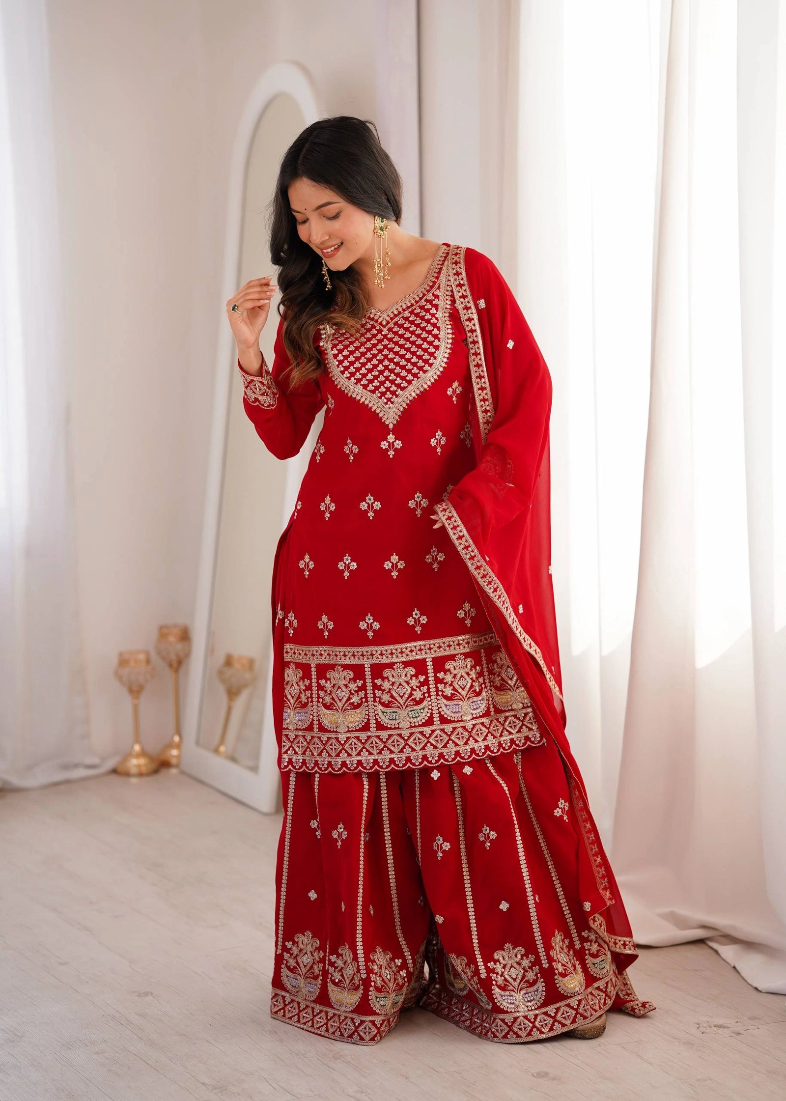 Woman in a red traditional outfit with white patterns standing in a well-lit room.