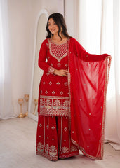 Woman in a red traditional outfit with white patterns standing in a bright room.