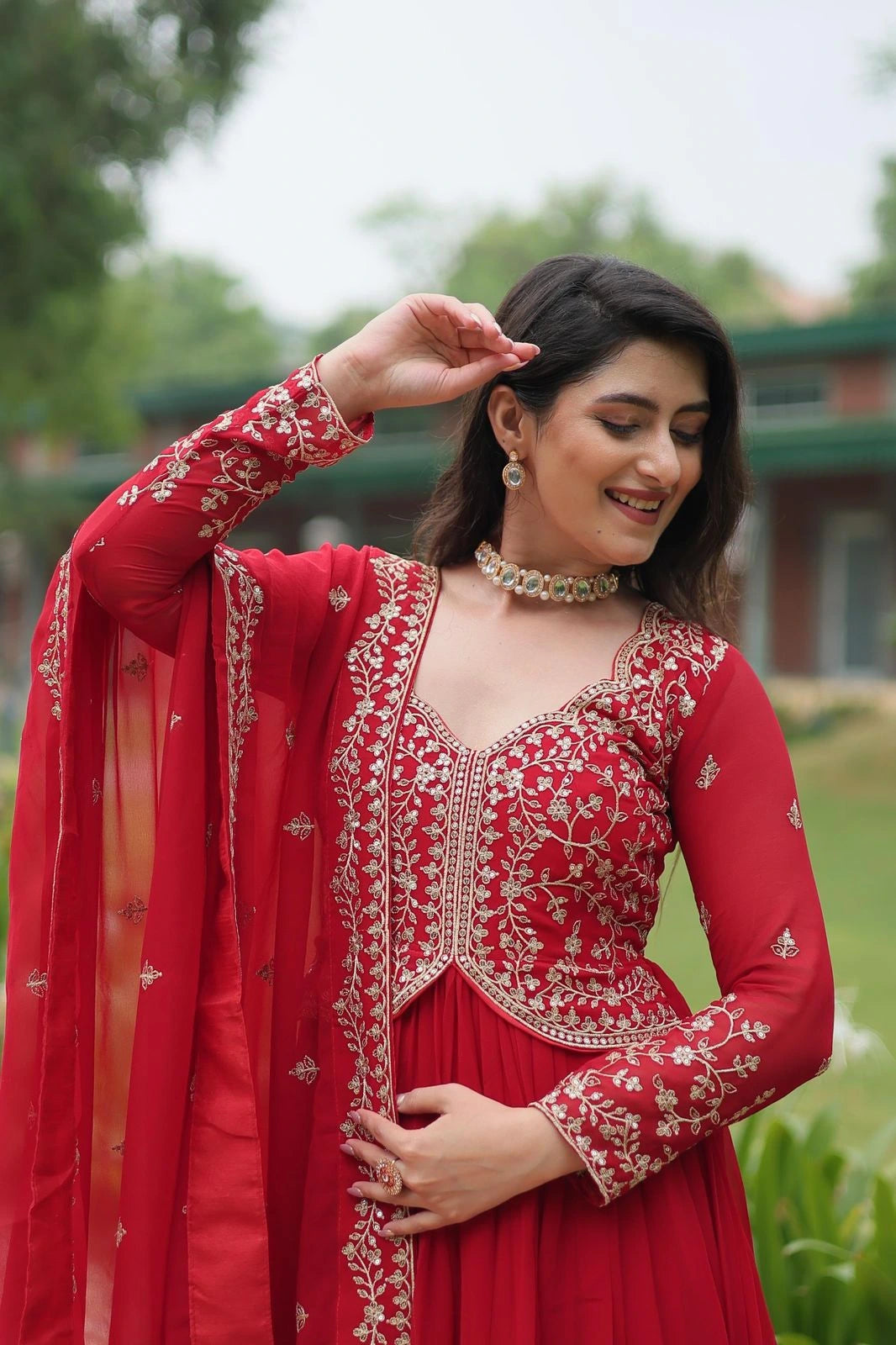 Woman in a red traditional outfit with intricate embroidery outdoors.
