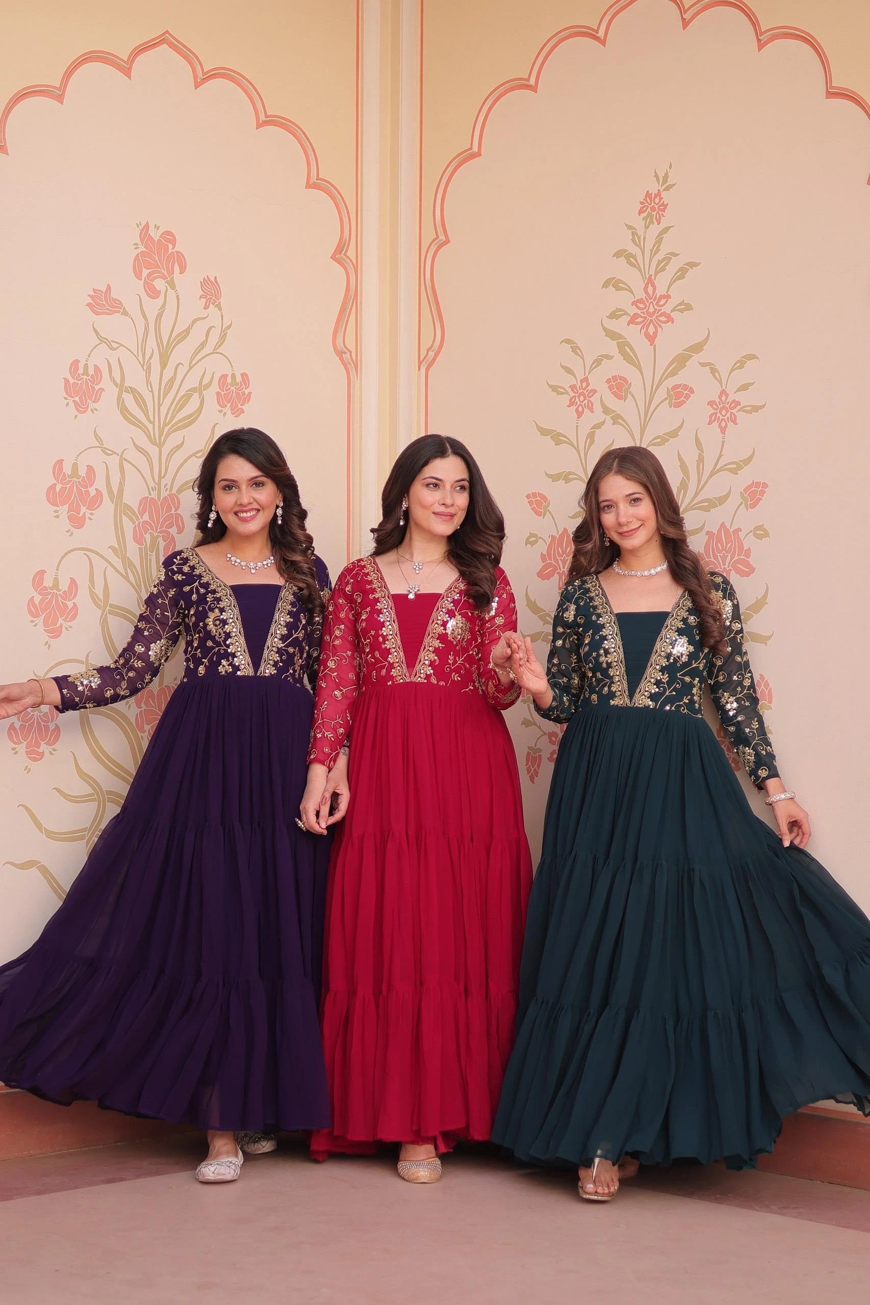 Three women in colorful traditional dresses standing against a decorative wall.