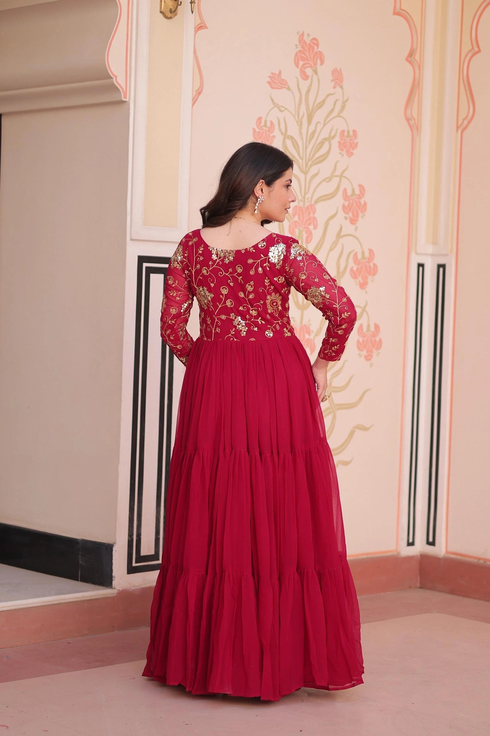 Woman wearing a red traditional outfit with floral patterns in an indoor setting.