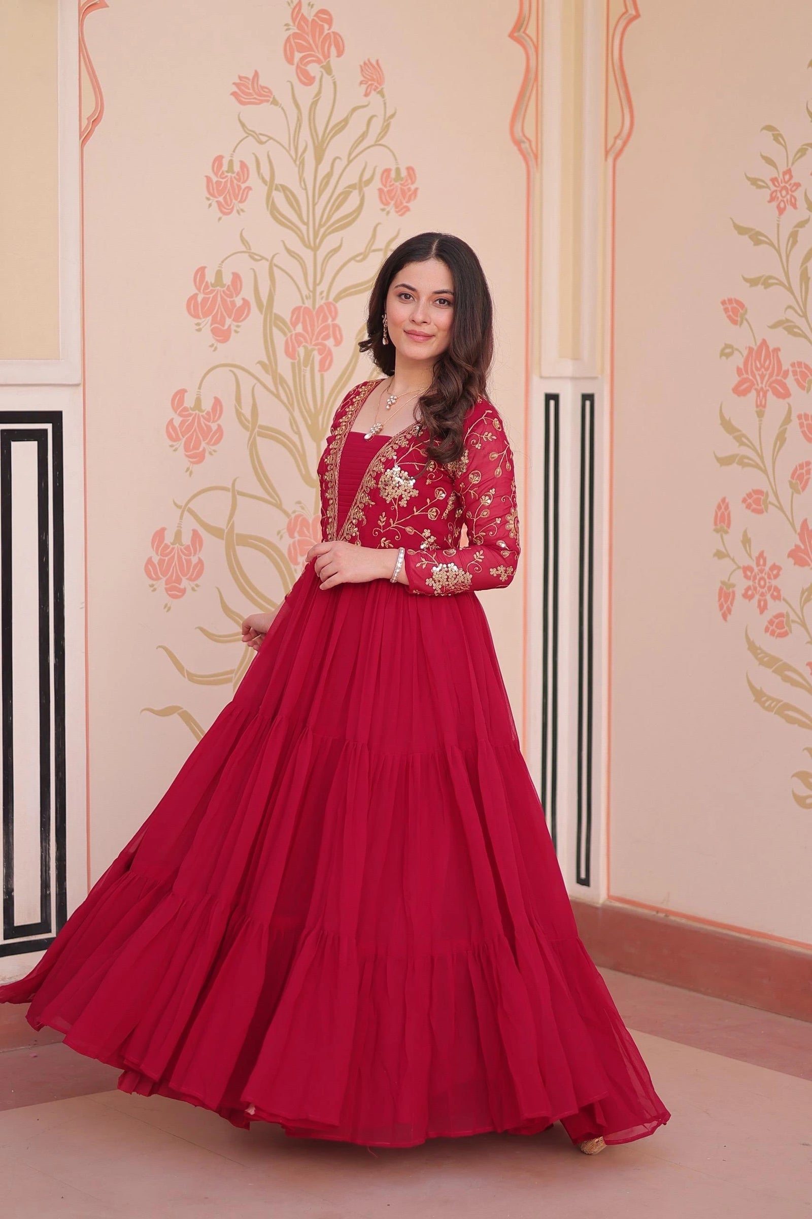 Woman wearing a red traditional outfit with gold details against a decorative wall.