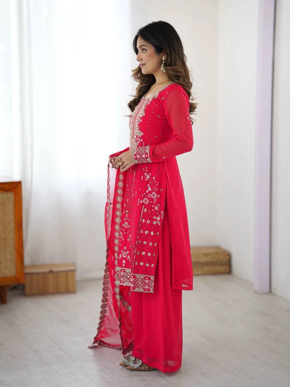 Woman wearing a bright pink traditional outfit with white embroidery in a minimalistic setting.