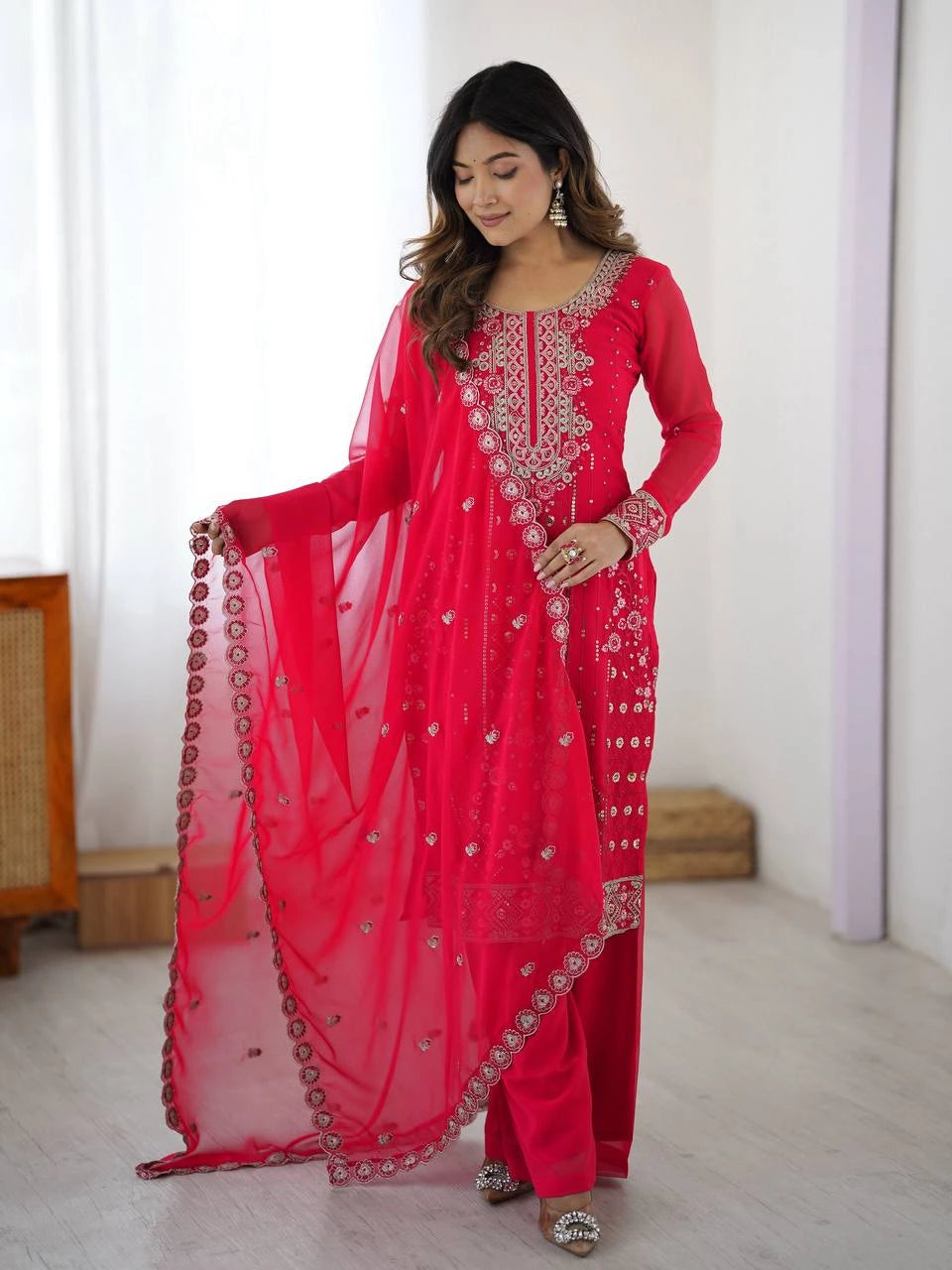 Woman wearing a bright pink traditional outfit with intricate designs indoors.