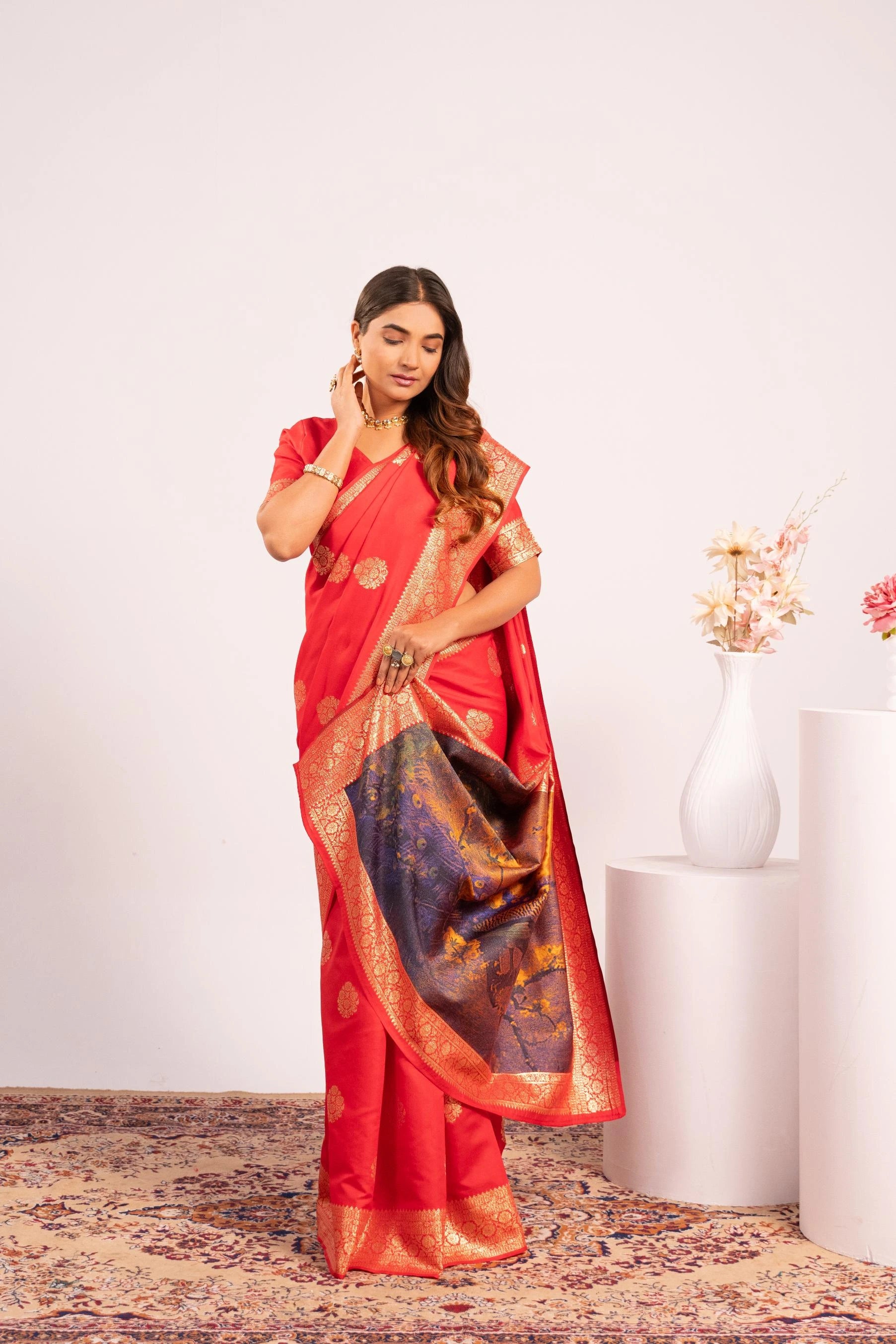 Woman in a red saree with gold border standing in a minimalistic room.