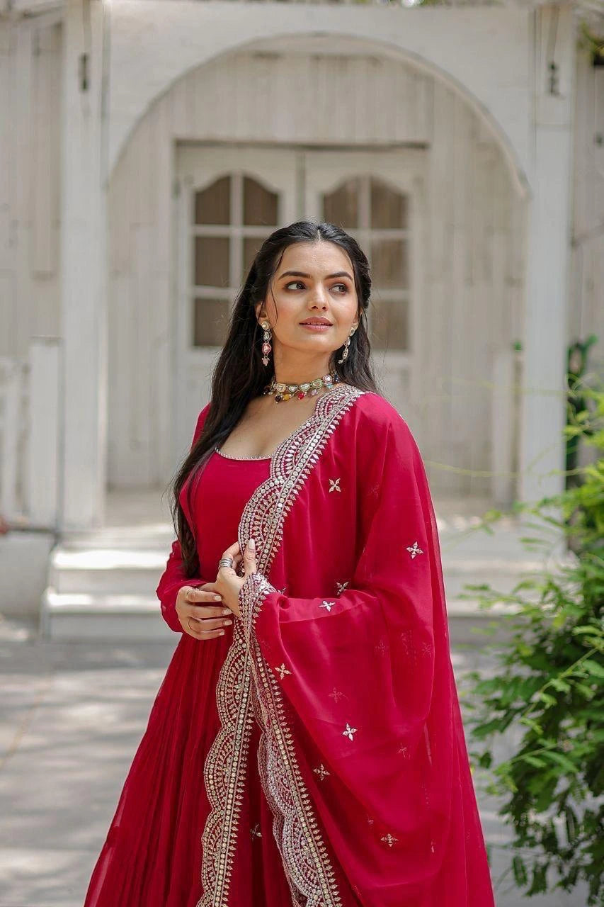 Woman in a red traditional outfit with intricate designs standing outdoors.