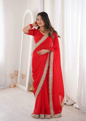 Woman wearing a red saree with gold border in a white room.