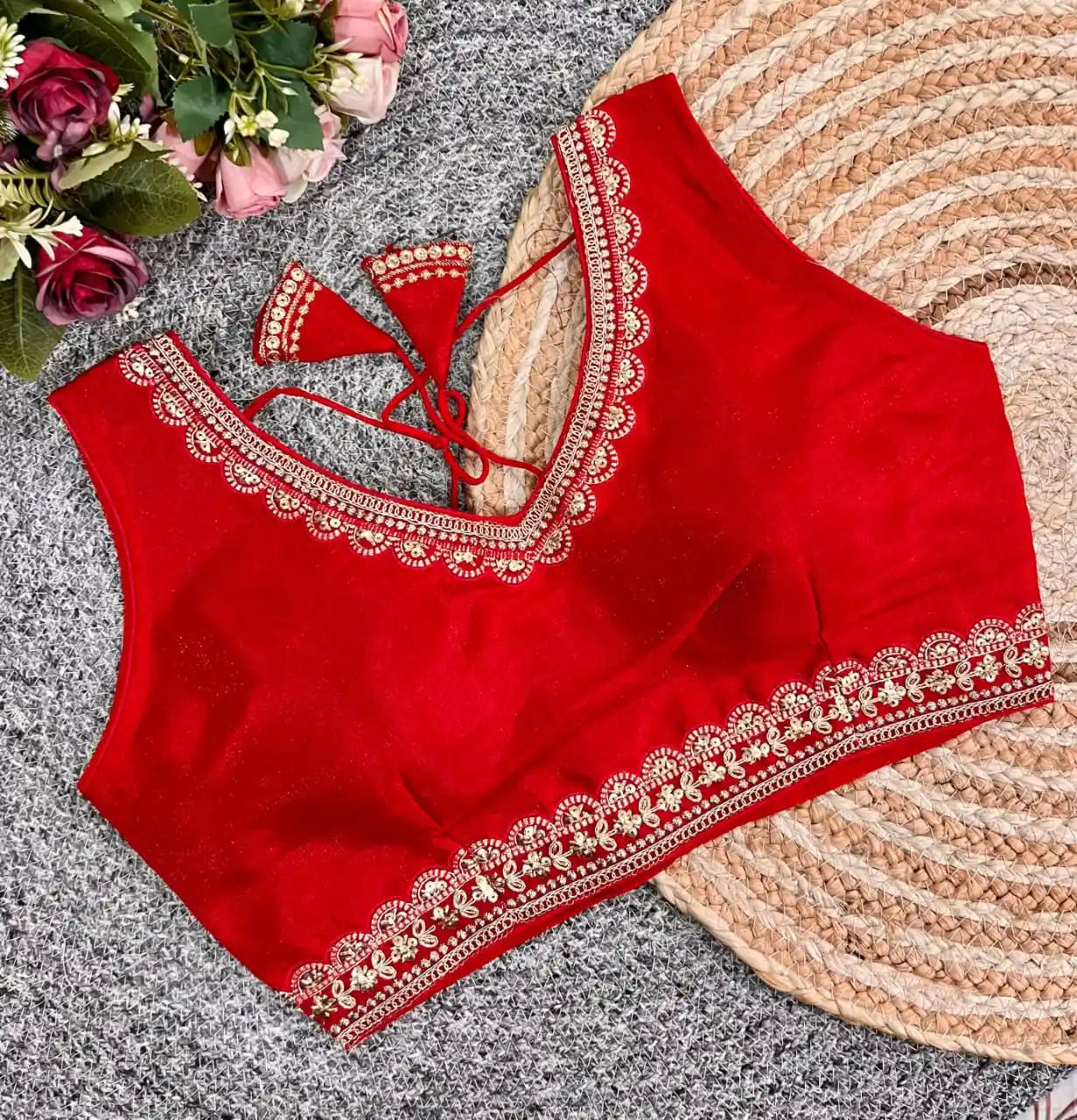 Red blouse with white embroidery on a textured surface with flowers in the background