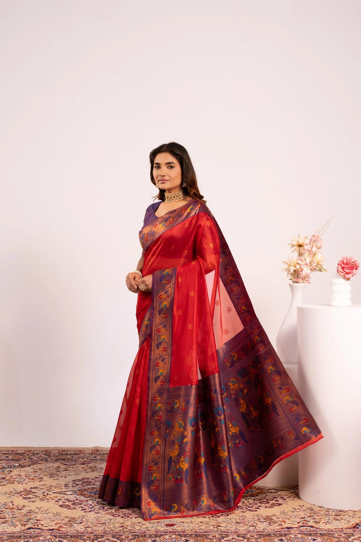 Woman wearing a red saree with a floral arrangement in the background