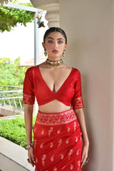 Woman wearing a red traditional outfit with a floral pattern, standing outdoors.